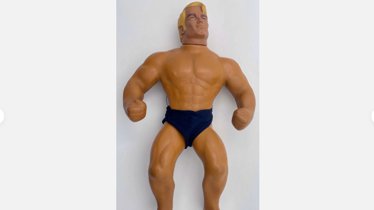 vintage Stretch Armstrong action figure, muscular build, blonde hair, wearing black trunks, posed against plain white background