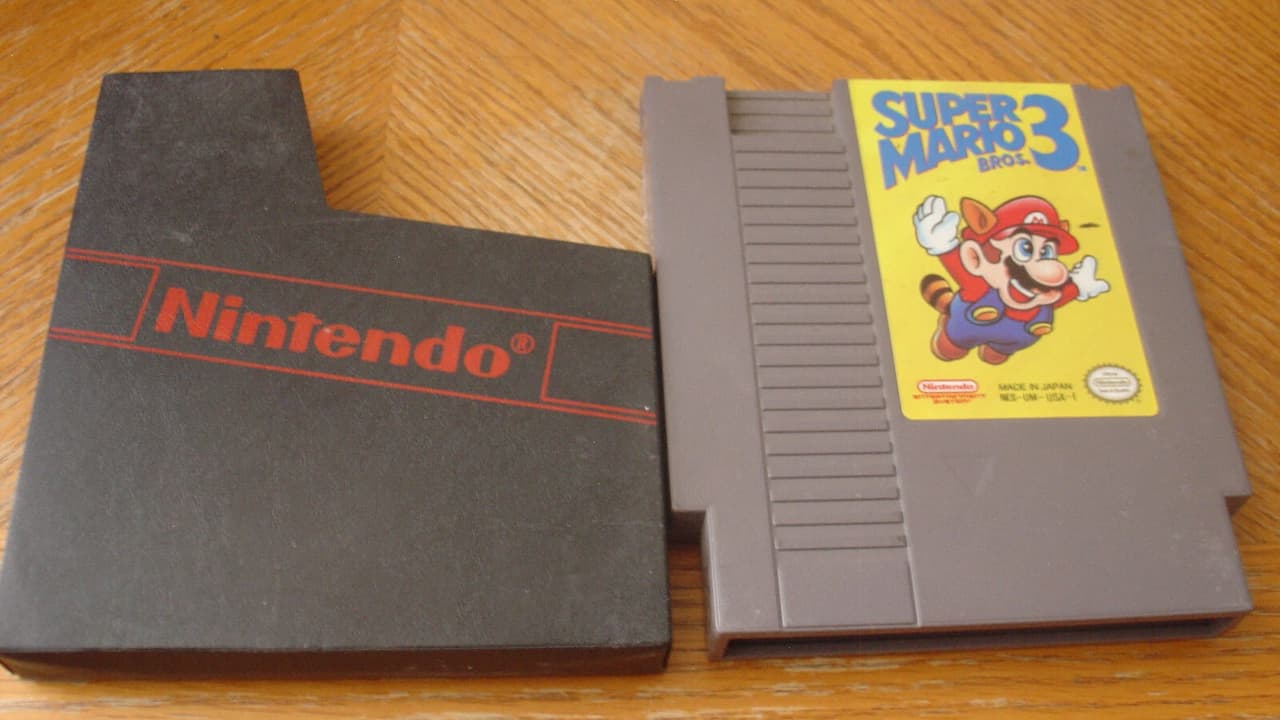 Super Mario Bros NES cartridge, rectangular gray plastic, label with Mario jumping over a pipe, red and blue graphics, iconic 8-bit video game cover