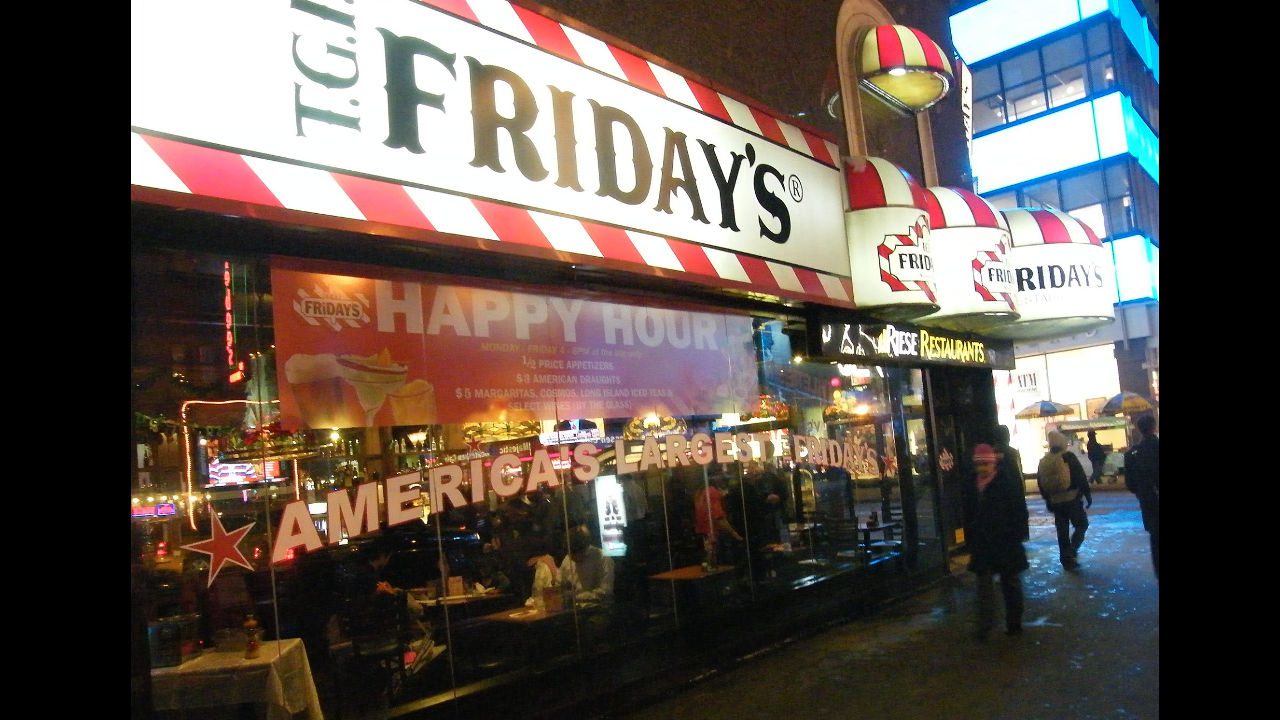 Exterior of a TGI Friday’s restaurant at night with bright signage and a visible happy hour banner