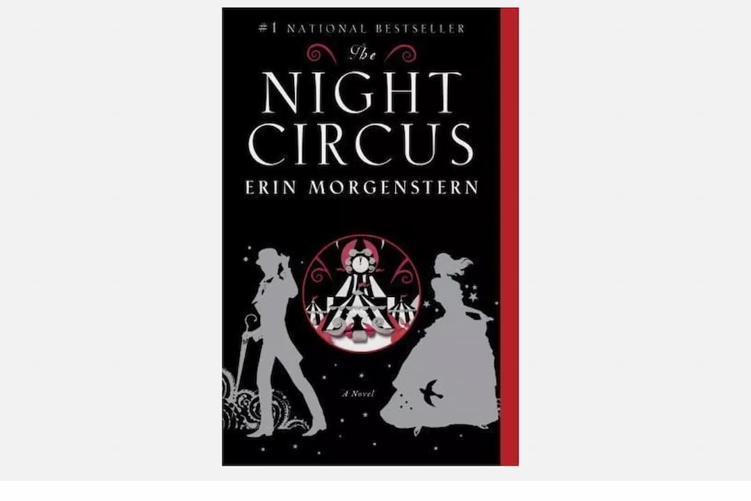 The Night Circus by Erin Morgenstern, paperback edition, black cover with white and red illustrations, stylized circus tent, silhouetted figures holding hands, ornate typography, author’s name in elegant script, published by Anchor Books