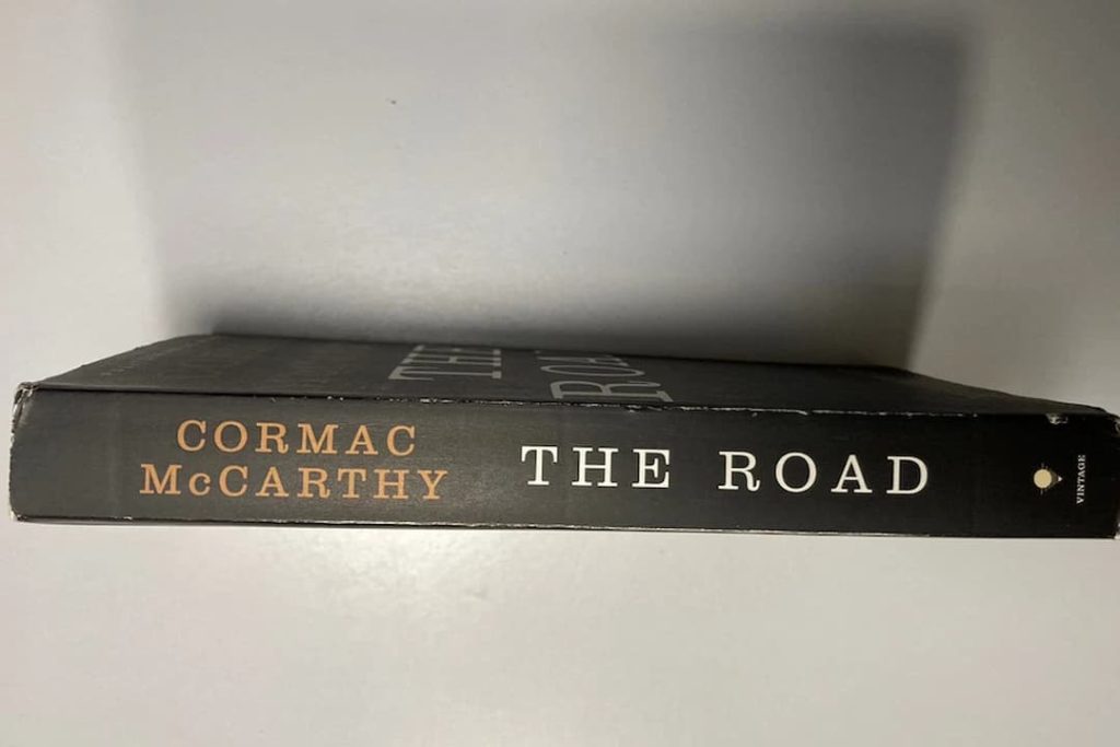 The Road by Cormac McCarthy, paperback edition, dark cover with minimalistic design, large bold white and red title text, author’s name in uppercase, Pulitzer Prize sticker, published by Vintage International