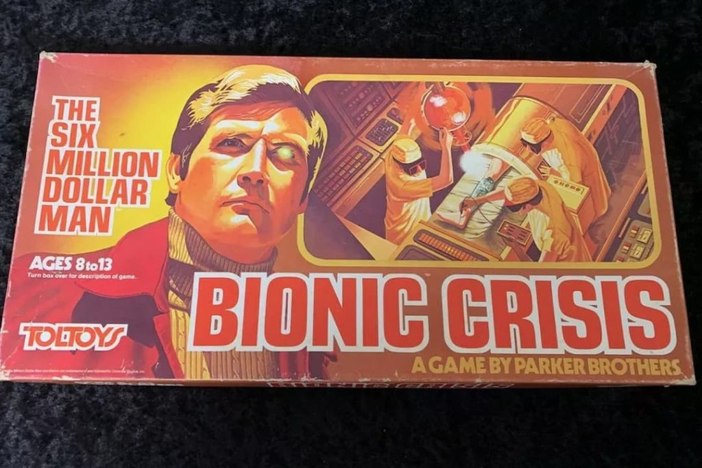 The Six Million Dollar Man Bionic Crisis board game box, featuring a bold illustration of Steve Austin, surgical team operating in a high-tech lab, red-orange color scheme, branding by Toltoys and Parker Brothers