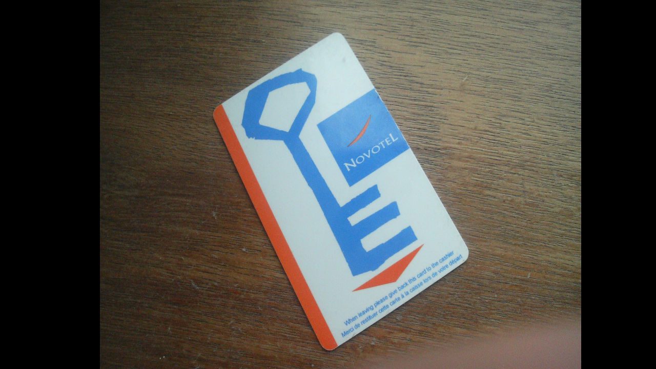 Novotel hotel key card placed on wooden surface, with red stripe and blue key-shaped logo