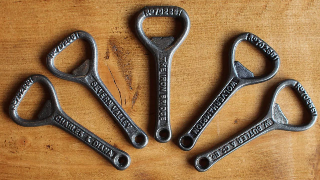 Five vintage metal bottle openers, labeled with place names, arranged in a fan shape on wooden surface