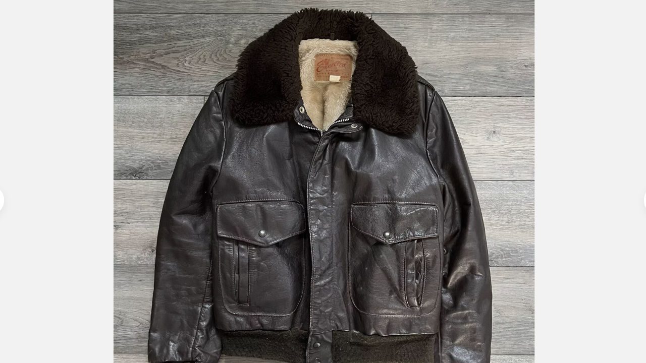 vintage leather bomber jacket, dark brown exterior, shearling collar and lining, large front pockets, displayed on wood background