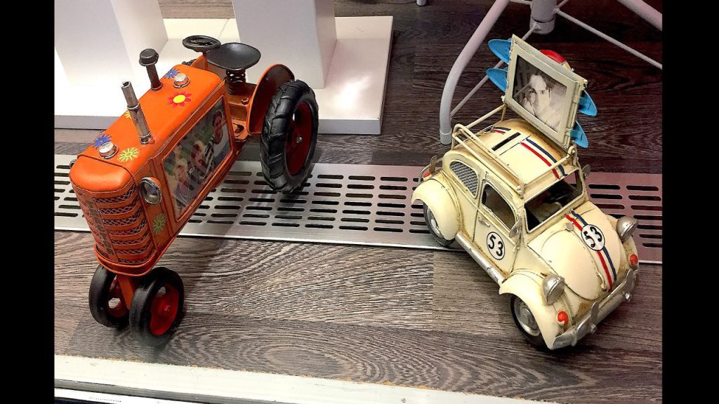 Vintage tin toy tractor and car, orange tractor with flower decals and photo frame, cream car with racing stripes and photo holder on roof, placed on wooden floor