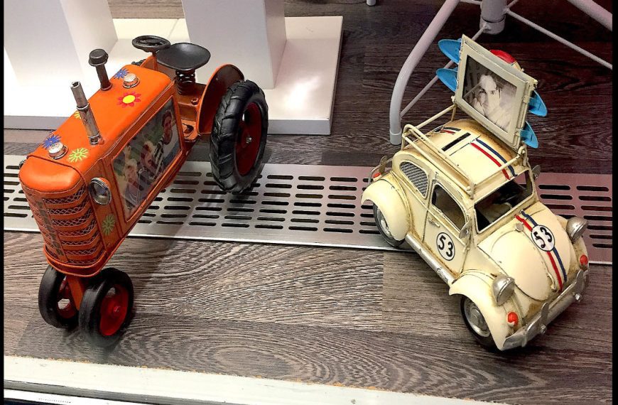 Vintage tin toy tractor and car, orange tractor with flower decals and photo frame, cream car with racing stripes and photo holder on roof, placed on wooden floor