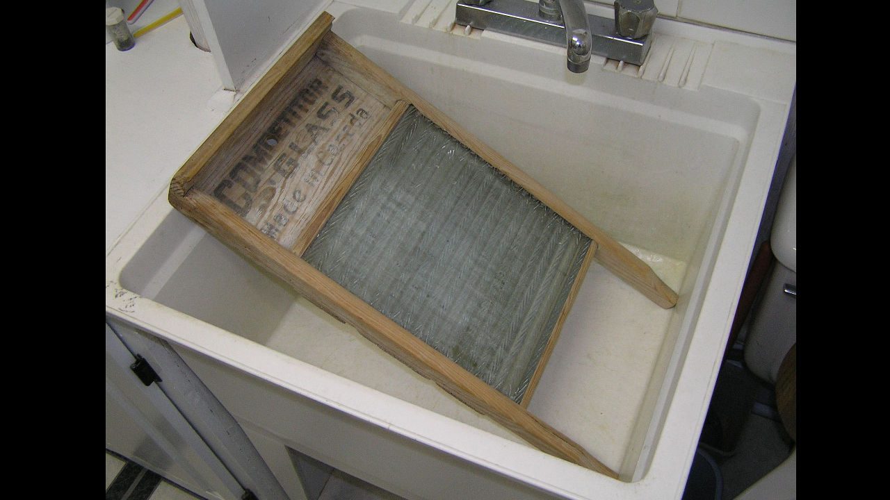 Vintage wooden-framed washboard placed inside a white laundry sink for hand-washing clothes