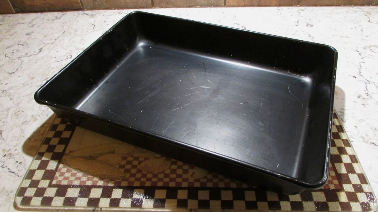 Black rectangular metal baking pan with visible scratches placed on a patterned kitchen counter