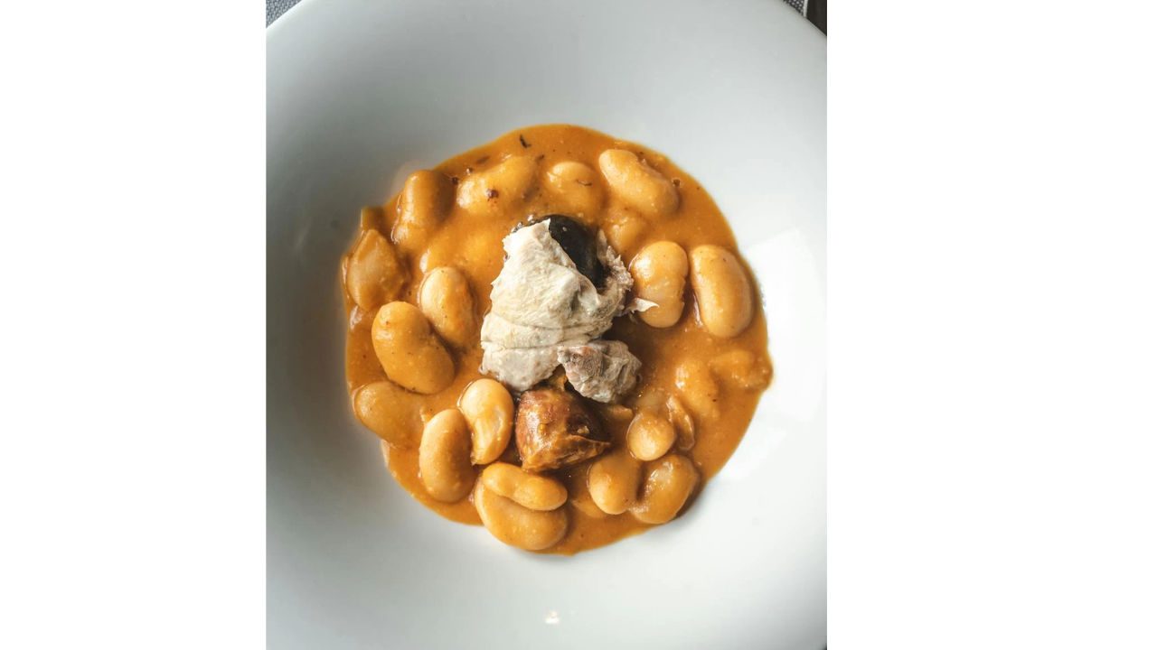 Plate of white beans in orange sauce topped with pieces of meat and sausage