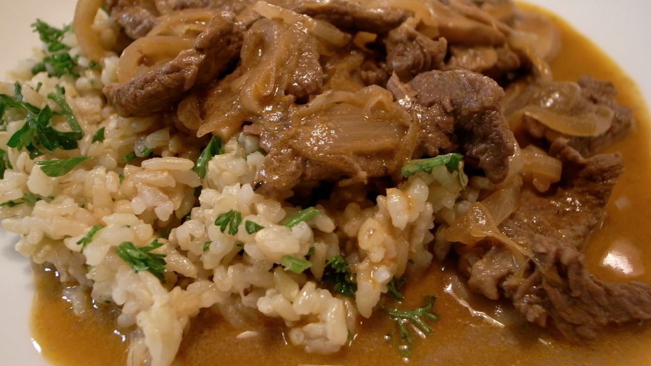 Close-up of beef stroganoff served over rice, garnished with chopped parsley and onions in sauce