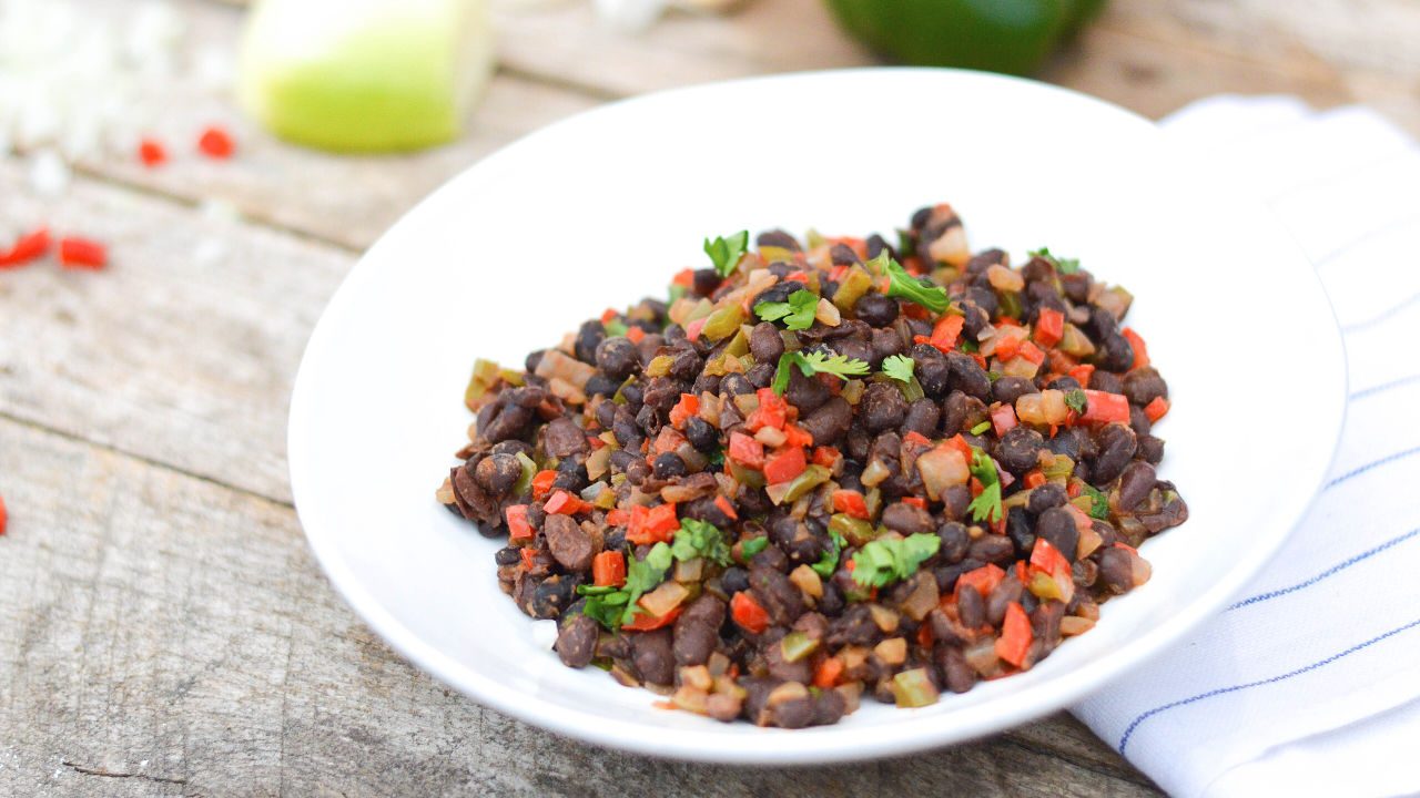 Cooked black beans with chopped red and green peppers, garnished with fresh cilantro, served on a white plate