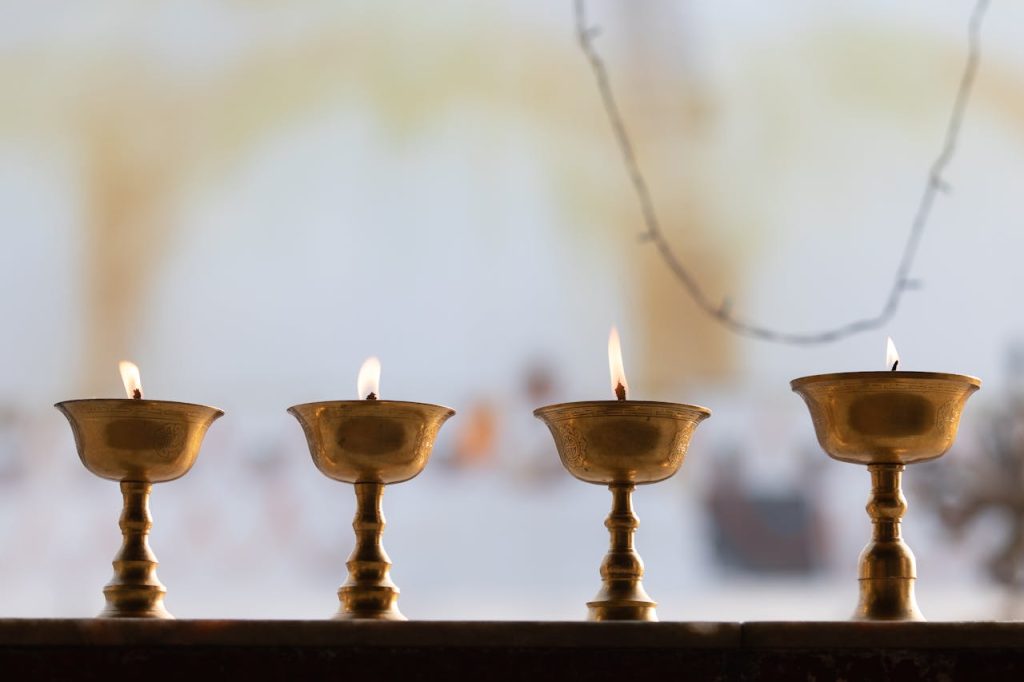 Five brass candle holders with small flames lit, arranged in a row on a flat surface