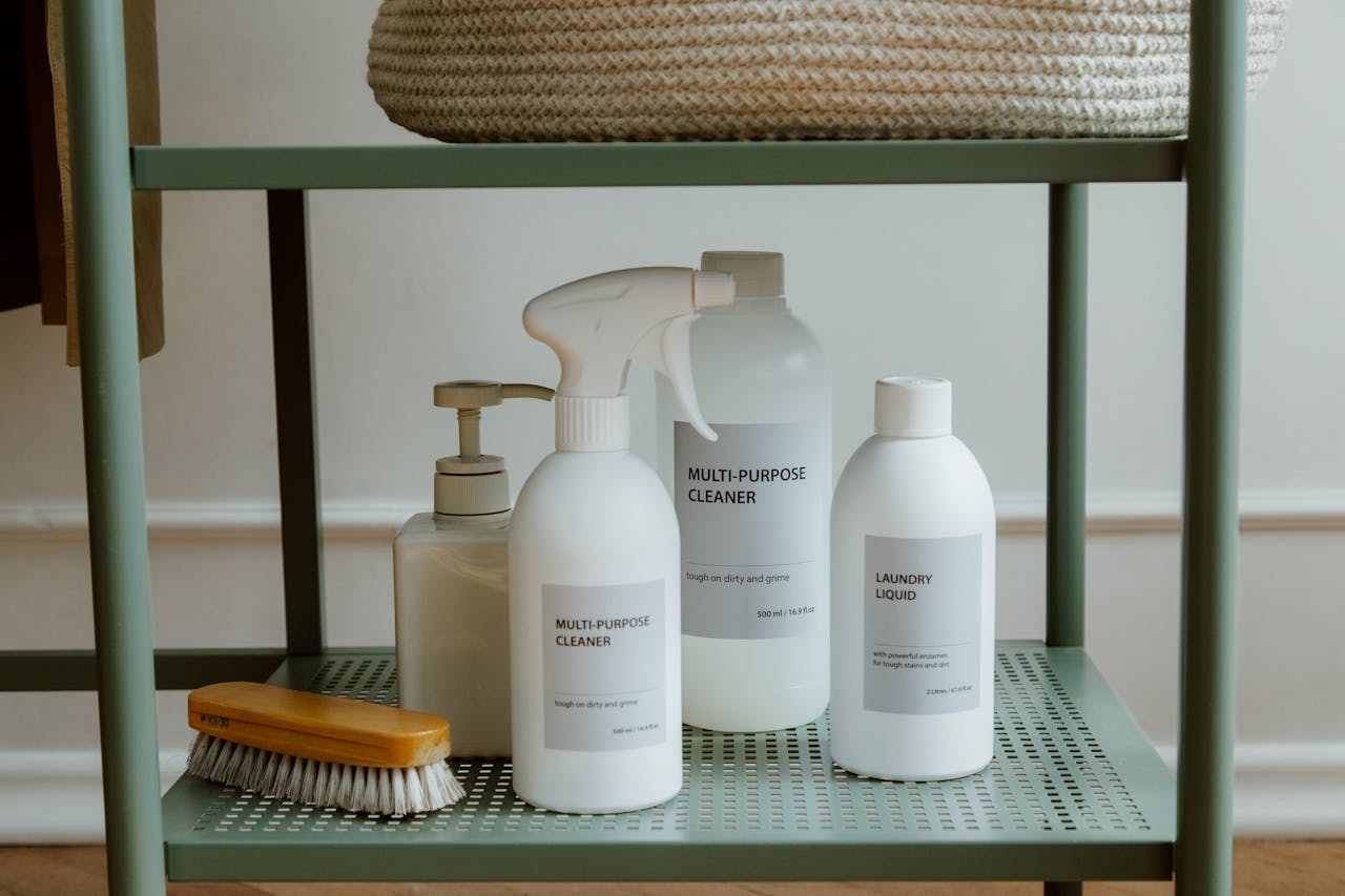Minimalist cleaning products and brush on shelf, including multi-purpose cleaner, laundry liquid, and soap dispenser