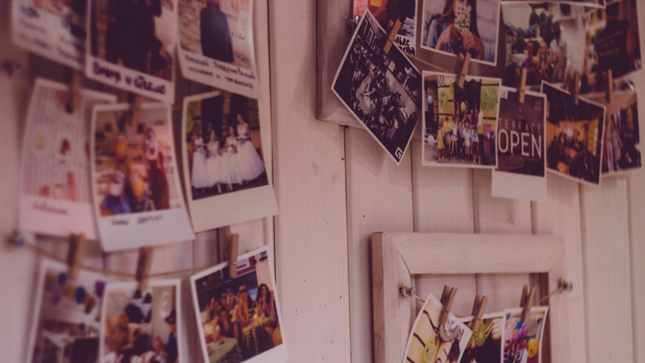 Close-up of a clothespin photo display on a wooden wall, featuring printed photos clipped to strings