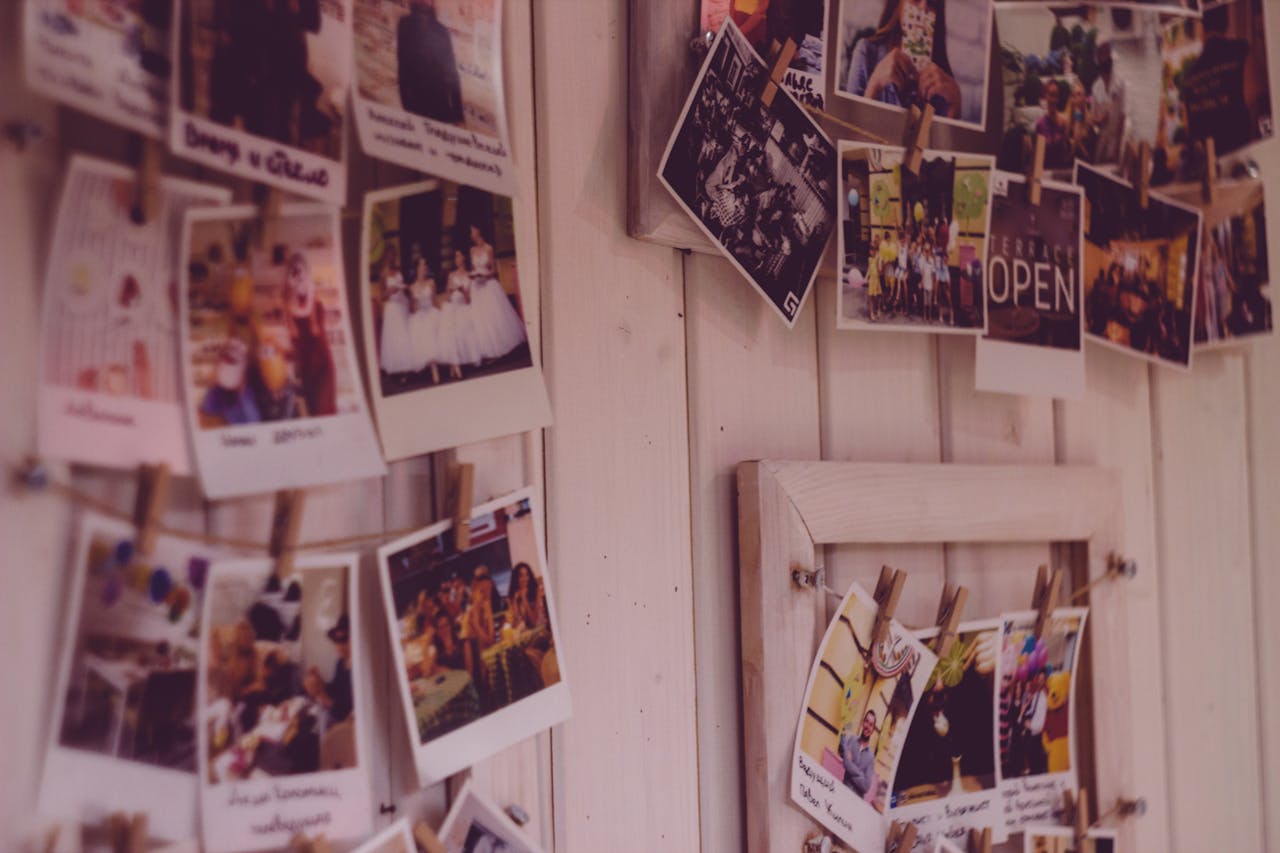 Close-up of a clothespin photo display on a wooden wall, featuring printed photos clipped to strings
