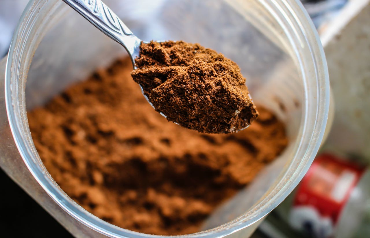 Spoonful of cocoa powder held over an open container filled with cocoa