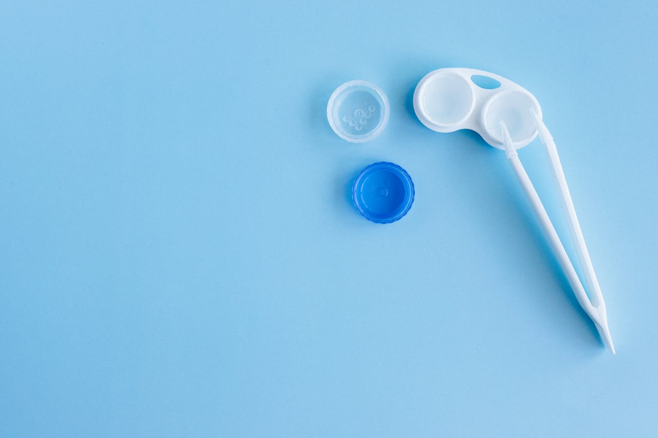  Contact lens case with open blue and clear lids, and white lens applicator on light blue background