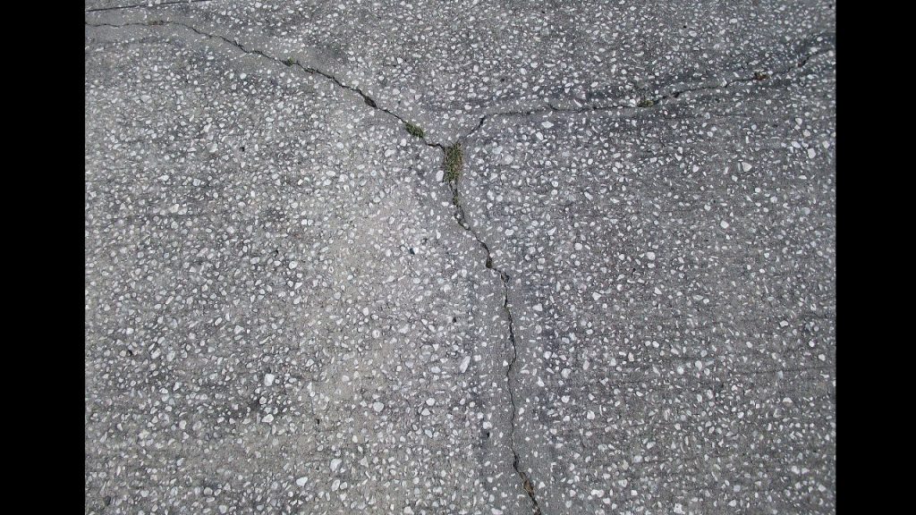 Cracked concrete surface with visible jagged lines and slight grass growth in the center split