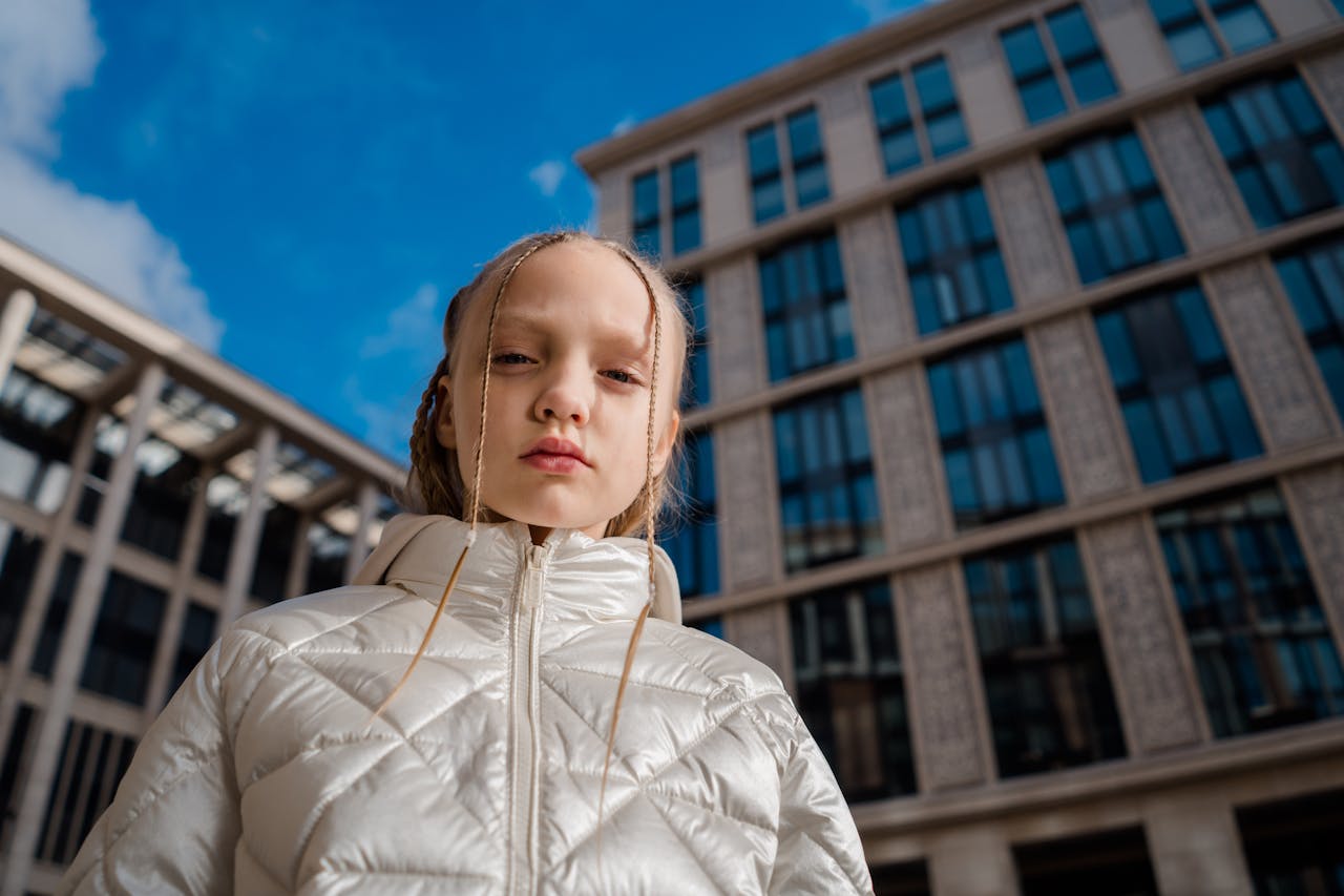 Young girl in shiny white down coat standing confidently in front of modern glass building