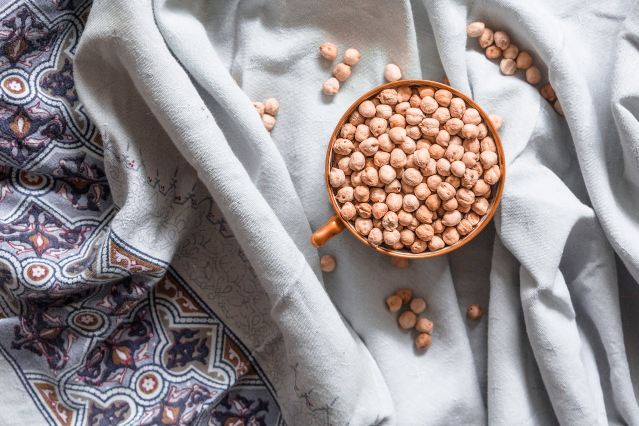Cup of dried chickpeas resting on light blue fabric with decorative patterns, some scattered around the cup