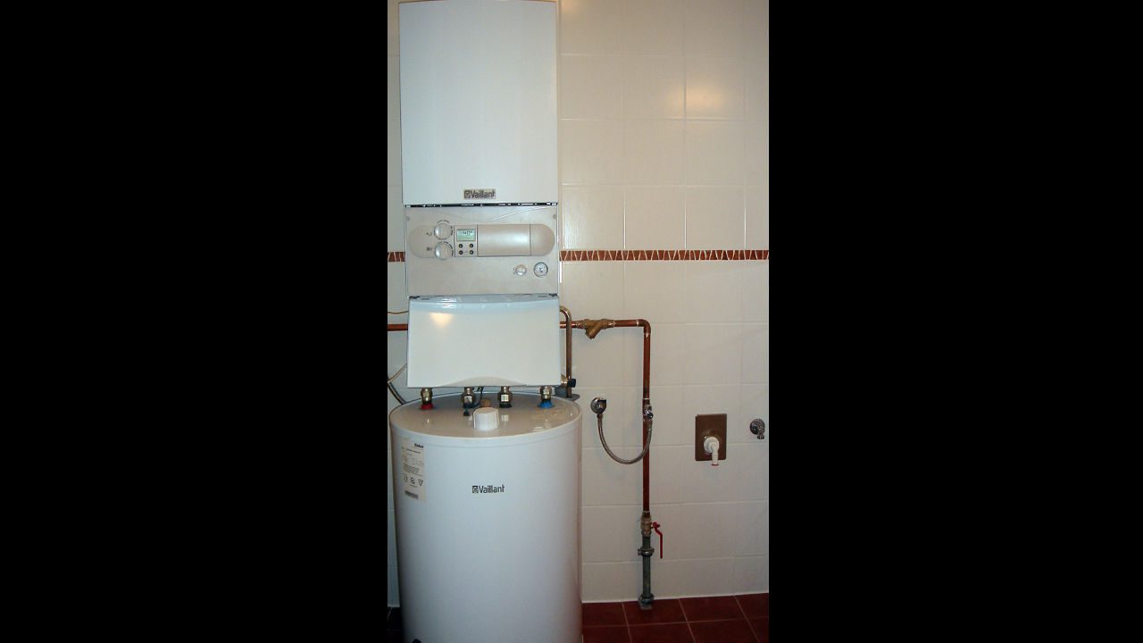Wall-mounted water heater and storage tank system with visible copper piping in a tiled utility room