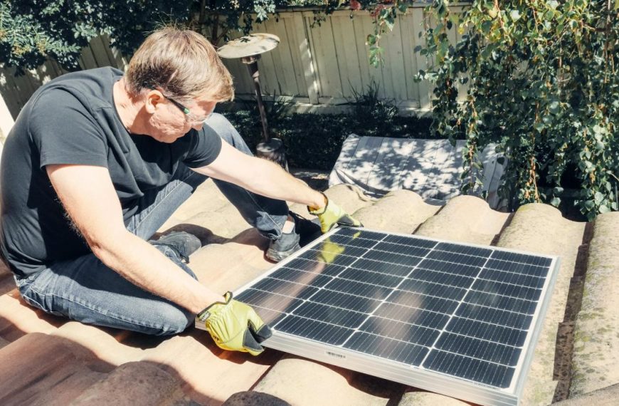 A Man in Black Shirt Sitting on the Roof while Holding a Solar Panel
