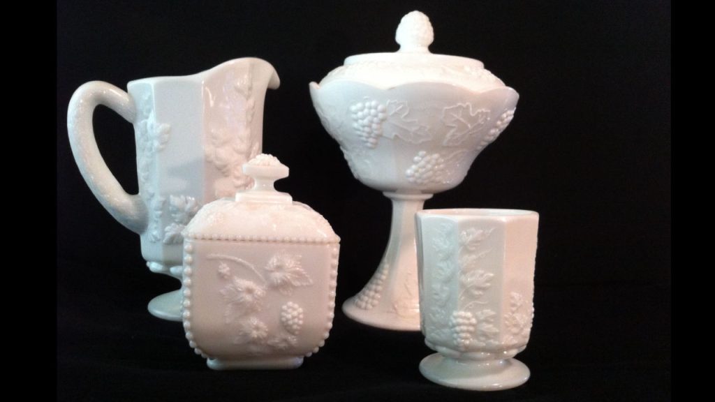 White milk glass dishes, embossed grapevine pattern, includes pitcher, goblet, sugar bowl, pedestal candy dish, black background