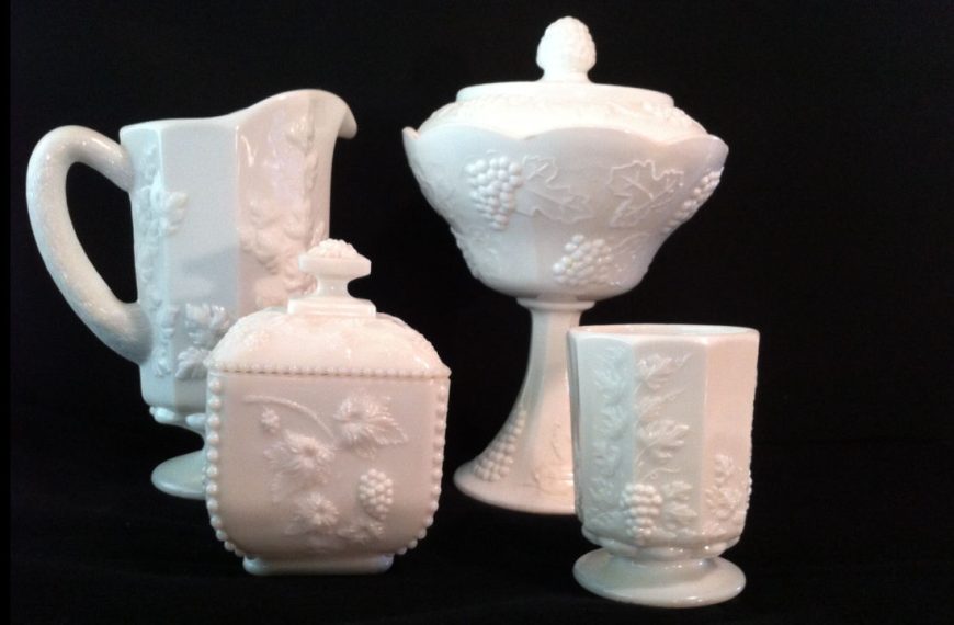 White milk glass dishes, embossed grapevine pattern, includes pitcher, goblet, sugar bowl, pedestal candy dish, black background
