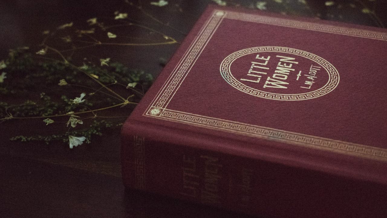 Red book with gold detailing on the cover, placed on a dark wooden surface, soft fairy lights in the background, partially blurred festive decor, cozy and warm ambiance