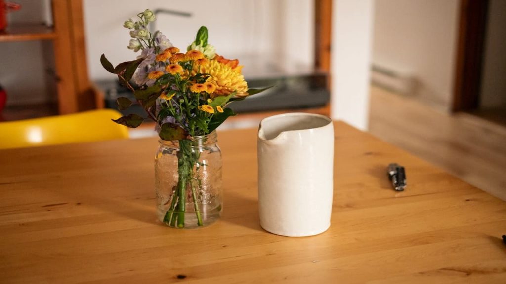 clear mason jar, used as vase, filled with fresh flowers, rustic style, twine tied around rim, placed on wooden surface, natural daylight