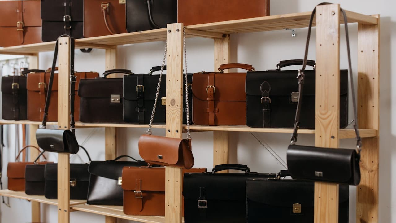 Bags on shelves, neatly arranged display, variety of styles and sizes, handbags and totes, leather and fabric materials, assorted colors and textures, retail store shelving, organized fashion accessories