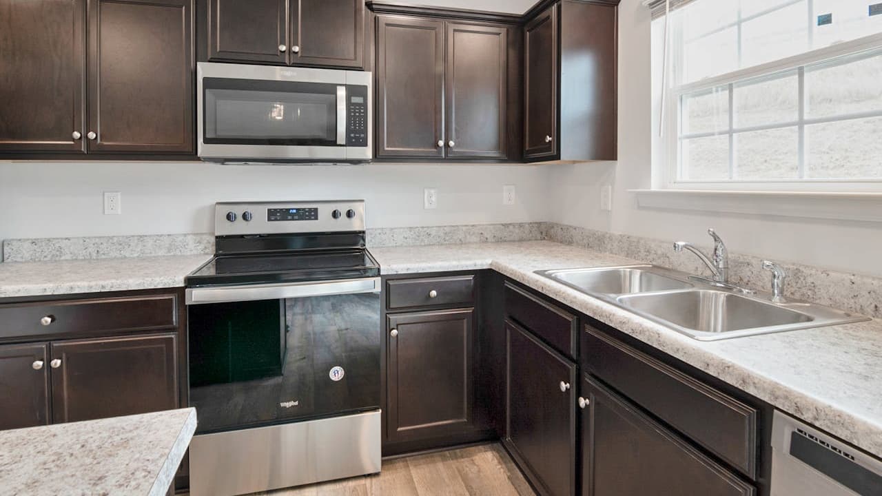 Modern kitchen interior, dark wooden cabinets, stainless steel appliances, electric stove with oven, mounted microwave, white tile backsplash, granite countertops, stainless steel sink, large window with natural light
