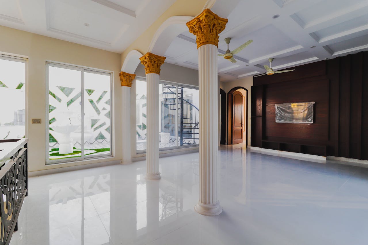 Bright room with gold-topped white columns, white glossy floor, wood accent wall, sliding doors, ceiling fans