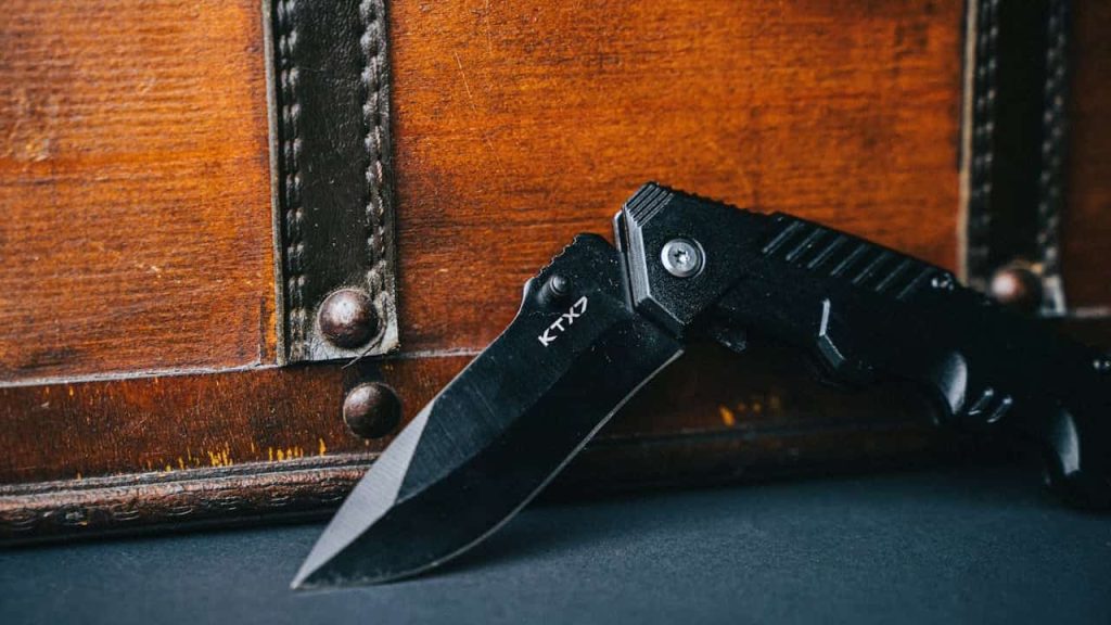 Black pocket knife, compact and foldable design, matte black handle, partially open stainless steel blade, ergonomic grip, placed on neutral background
