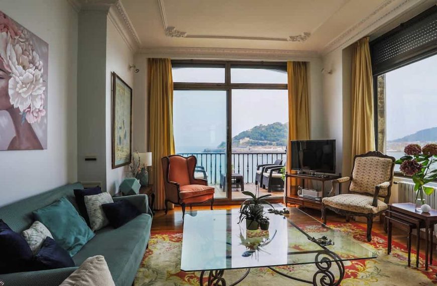 Furniture obstructing pathways in a living room, oversized couches, coffee tables, chairs crammed together, limited walking space, cluttered floor with scattered items, dim ambient lighting