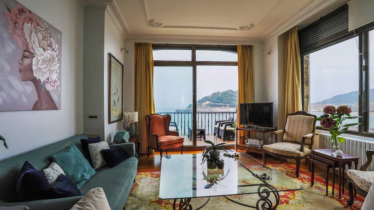 Furniture obstructing pathways in a living room, oversized couches, coffee tables, chairs crammed together, limited walking space, cluttered floor with scattered items, dim ambient lighting