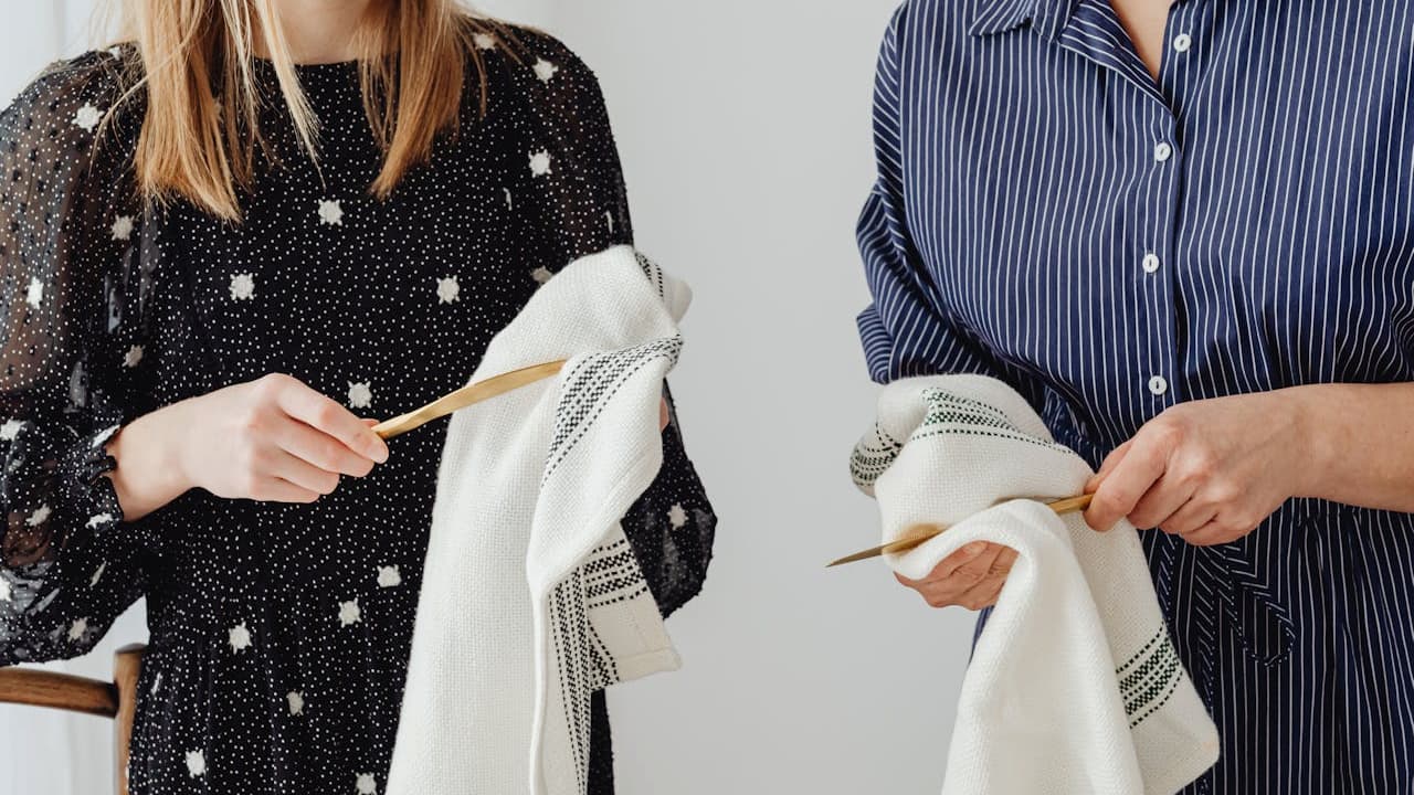 Two people drying dishes with cloth towels, holding utensils, partial view of torsos, casual clothing.