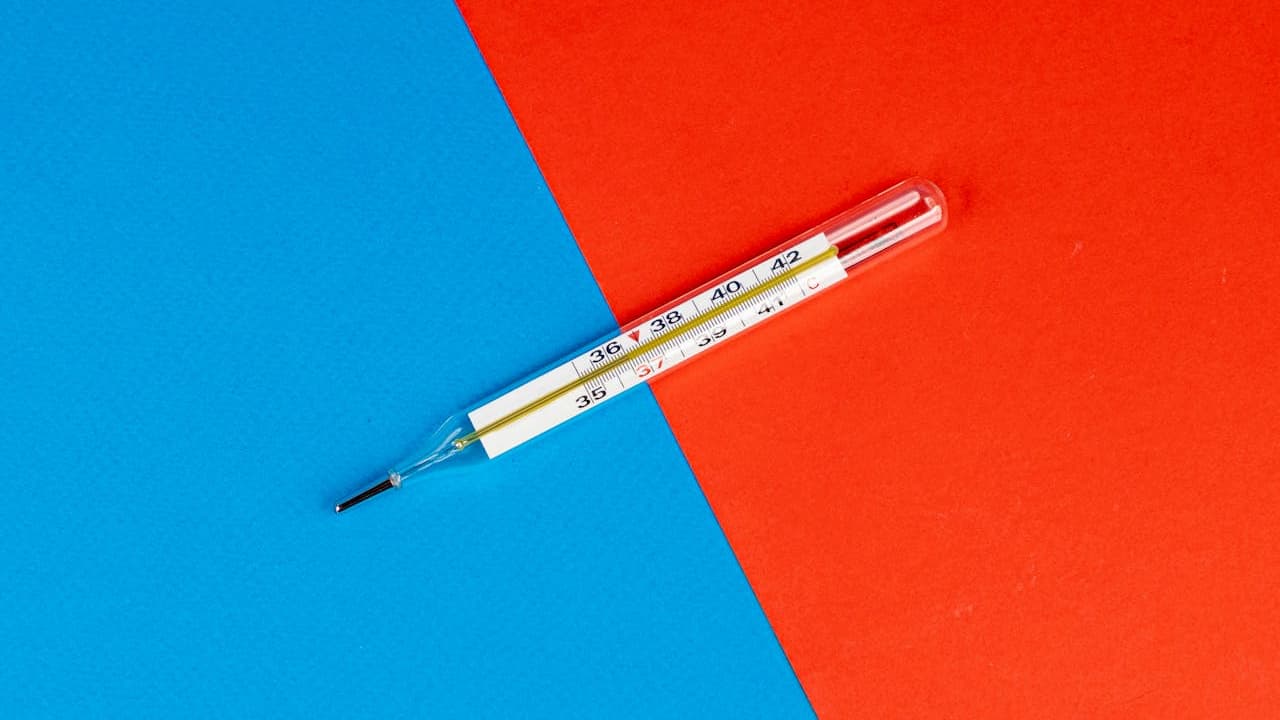 Glass thermometer, placed diagonally, blue and red background, silver tip, numeric scale visible, healthcare object, contrast color theme