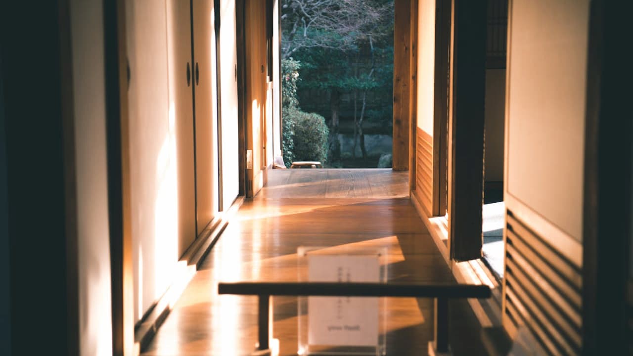 arrow hallway, wooden floors, sliding doors on both sides, soft natural light, view of greenery through open doorway, traditional interior style