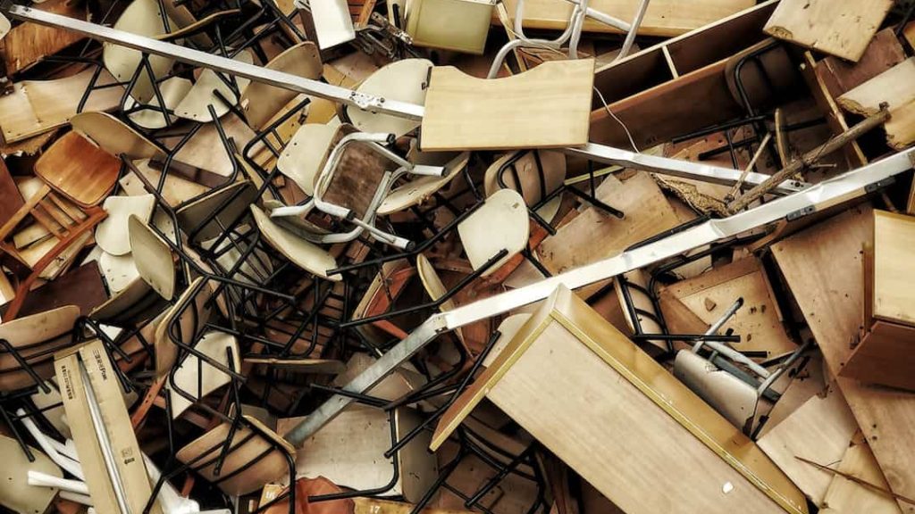 Heavy furniture piled on each other, wooden dressers, bulky sofas, chairs stacked haphazardly, visible dust, worn upholstery, dimly lit indoor space