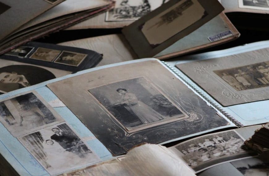 Open vintage photo albums spread out on a table, sepia and black-and-white portraits mounted on blue pages, handwritten notes beside some photos, delicate preservation materials nearby, nostalgic atmosphere of memory keeping