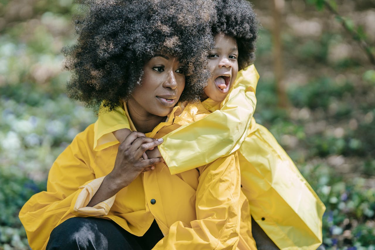 Mother and child in matching yellow raincoats embracing outdoors, child smiling playfully