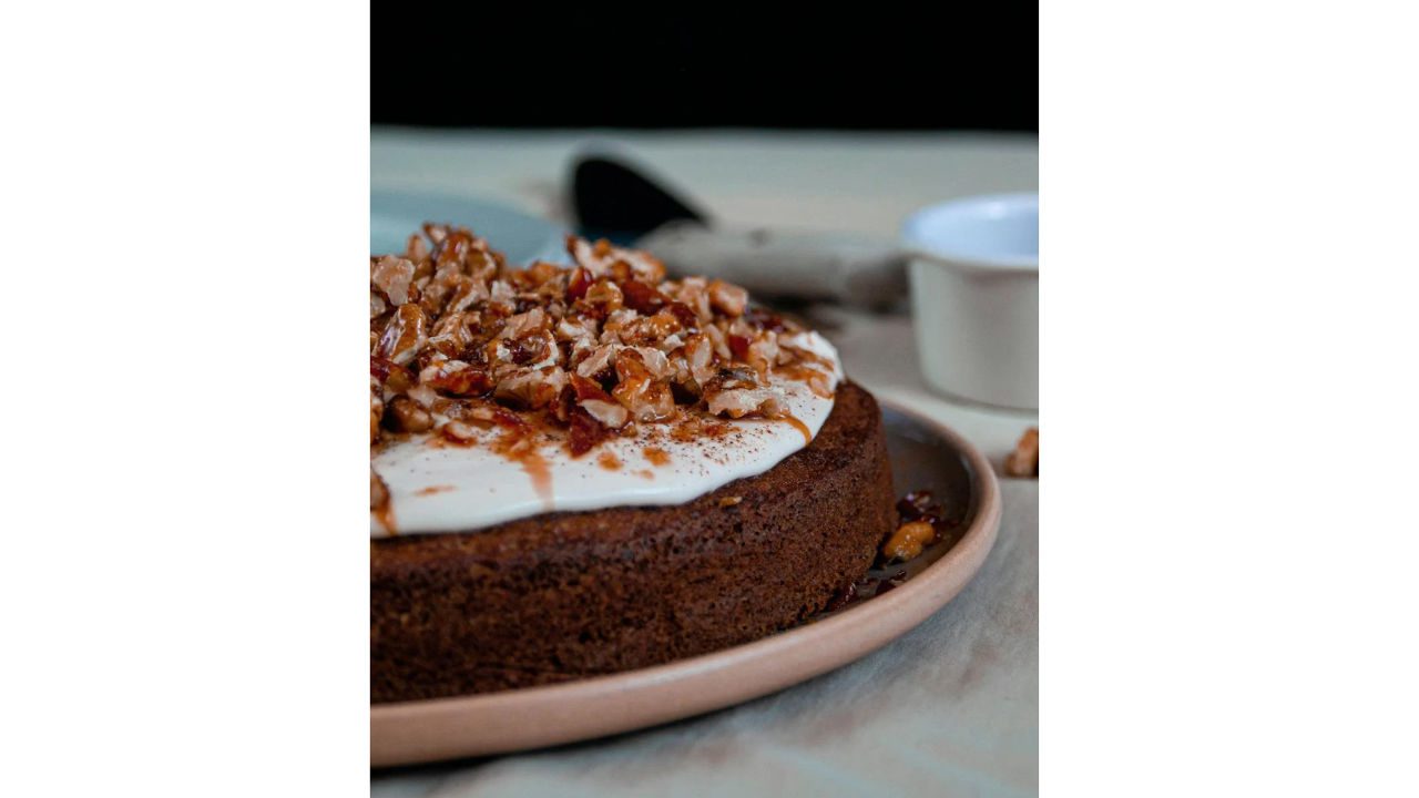 Spiced cake topped with white frosting, chopped nuts, and caramel drizzle on a brown ceramic plate
