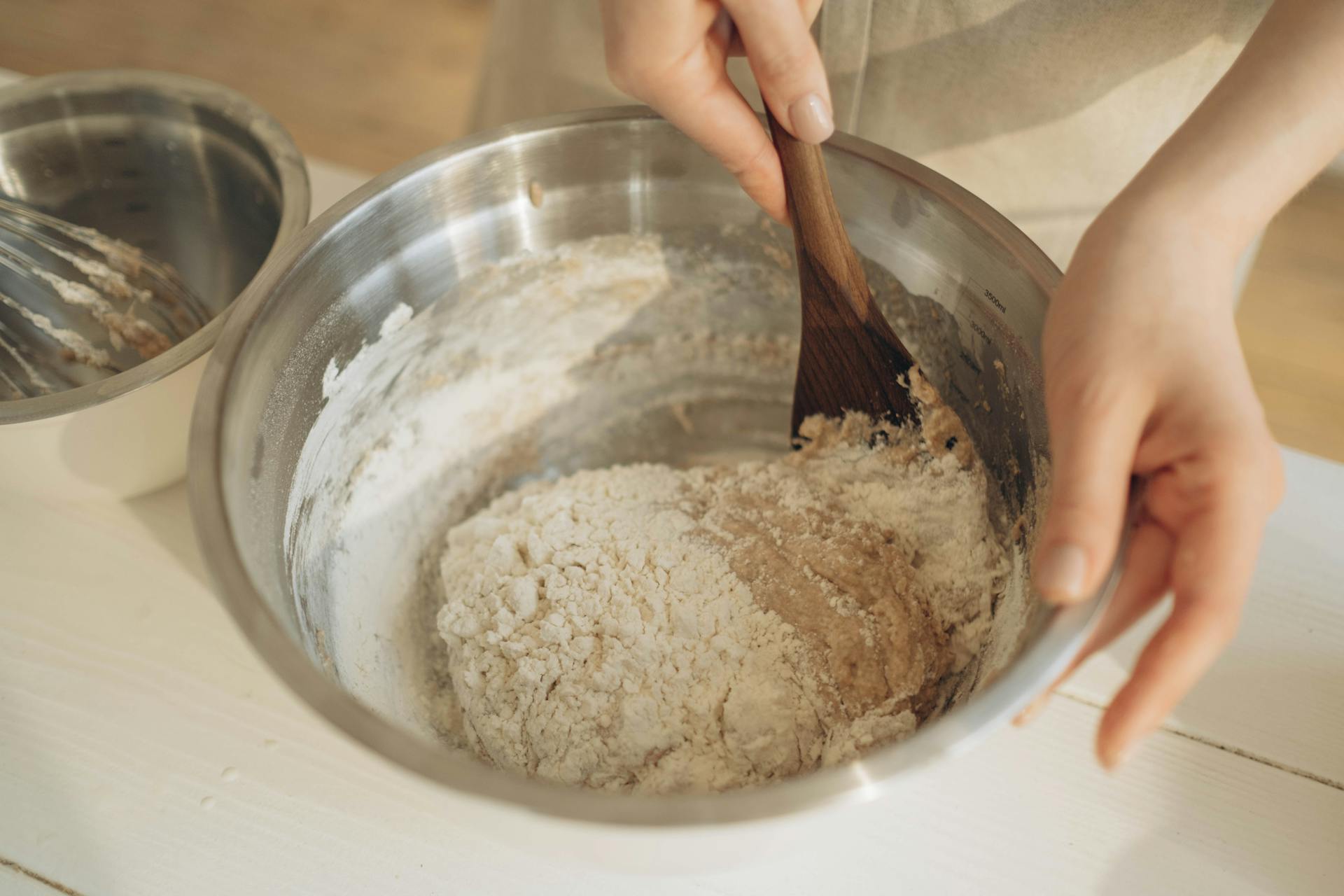 A Person Mixing the Dough Using a Wooden Spatula in a Stainless Bowl