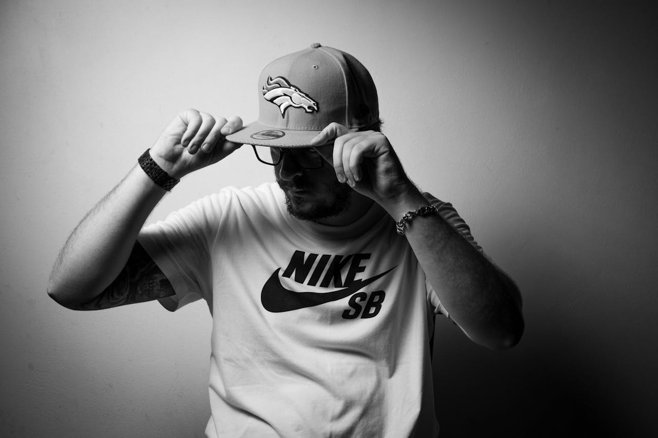 Man wearing a Nike SB t-shirt and a Denver Broncos cap, adjusting the brim with both hands