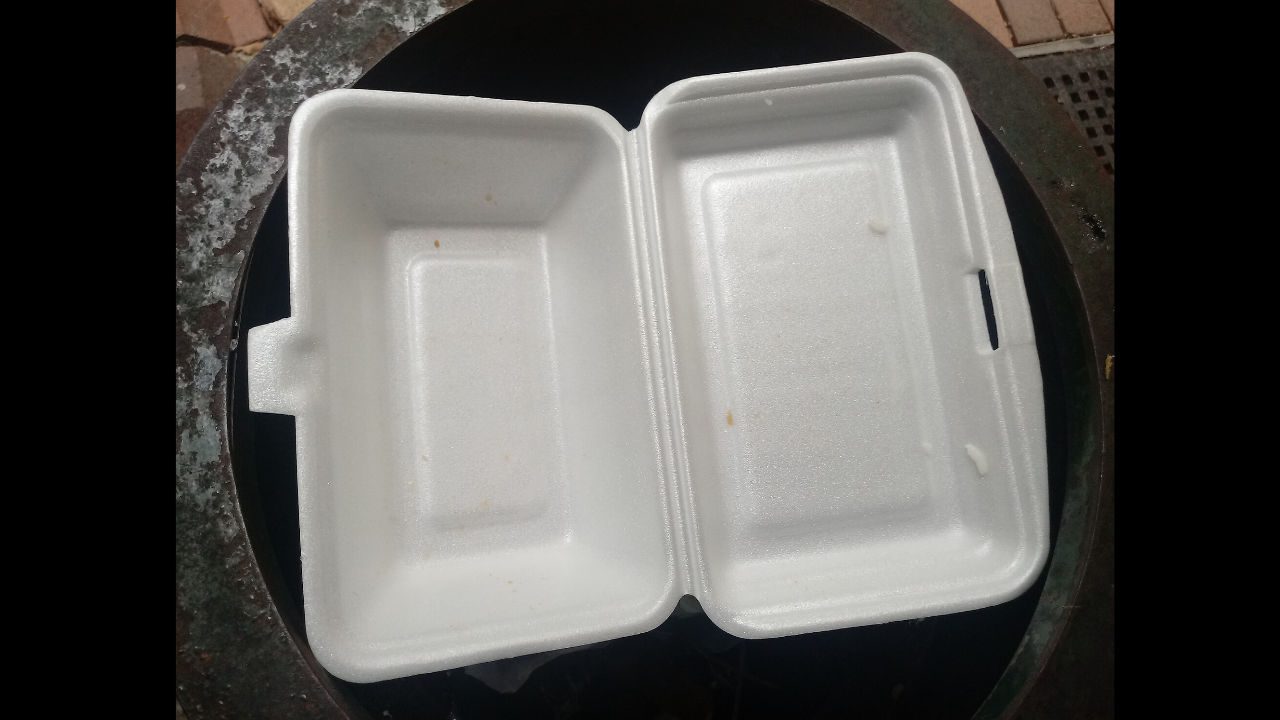 Empty white styrofoam take-out container placed inside a trash bin
