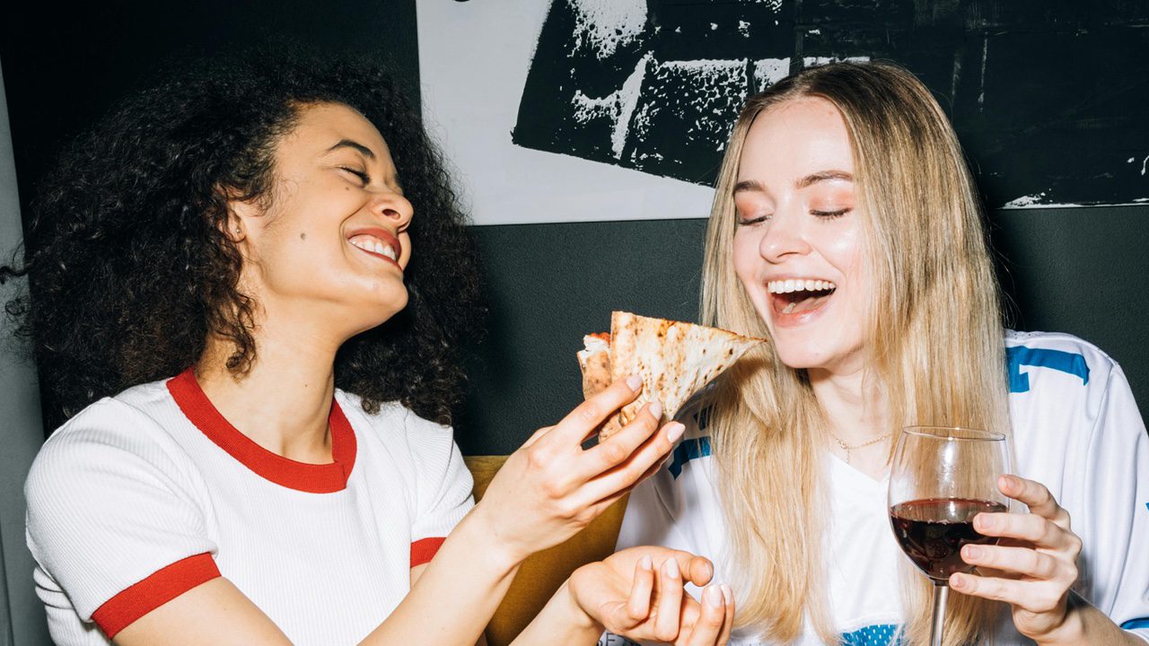 Two women friends eating snacks and drinking wine together