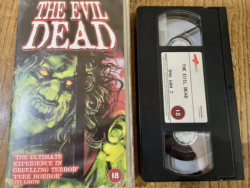 The Evil Dead 1983 Palace Explosive VHS, striking red and black cover, woman being dragged by unseen force, horror film label with "Palace Explosive" branding, clamshell case and tape visible