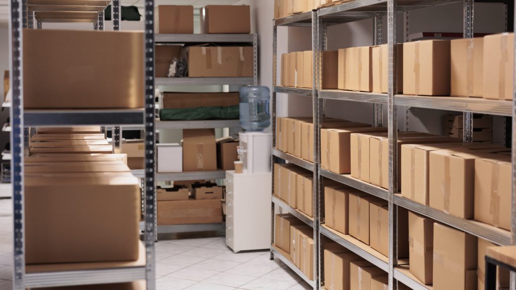 Storehouse interior with stacked cardboard boxes on tall metal racks. Goods cardboard boxes on shelves ready for transportration in industrial warehouse building with nobody inside Rent Storage Space